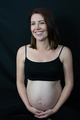 Caucasian pregnant woman against black backdrop, with copy space.