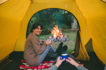 couple resting in tent with view on fire. woman drinking hot tea