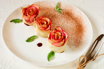 Аpple rose tarts on the white plate decorated mint leaves and cinnamon powder. Vegetarian autumn dessert on the white background. Top view