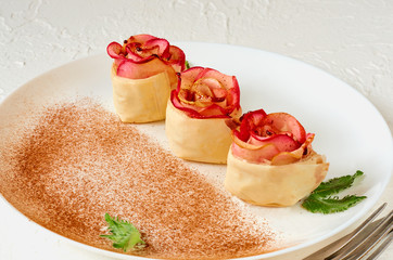 Mini apple rose pies on the white plate decorated mint leaves and cinnamon powder. Vegetarian autumn tart on the white background. Close up view