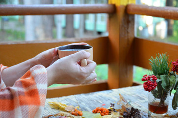 women's hands hold a cup of hot drink, Autumn, fall leaves, hot steaming cup of coffee and a warm scarf on wooden table background. Seasonal, morning coffee, Sunday relaxing and still life concept.