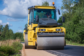 Yellow heavy vibration roller at asphalt pavement works. Road repairing in city. Road construction workers repairing highway road on sunny summer day. Heavy machinery, loaders and trucks
