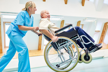 Pflegekraft und Senior im Rollstuhl albern herum