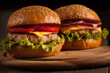 Home made hamburger with beef, onion, tomato, lettuce and cheese. Fresh burger close up on wooden rustic table with potato fries, beer and chips. Cheeseburger.