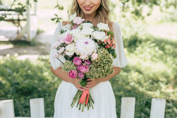 cropped shot of happy blonde bride holding beautiful wedding bouquet outdoors
