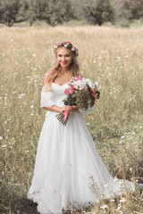 Fototapeta na wymiar high angle view of beautiful young bride holding bouquet and smiling at camera while standing on blooming field