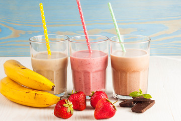 Long glasses of milkshakes with chocolate, strawberry, banana, with ice cream on white and blue background. Shakes and smoothies. Milk shake and cocktail for summer.