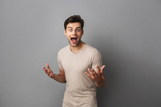 Photo of positive young guy 30s gesturing and screaming with delight, isolated over gray background