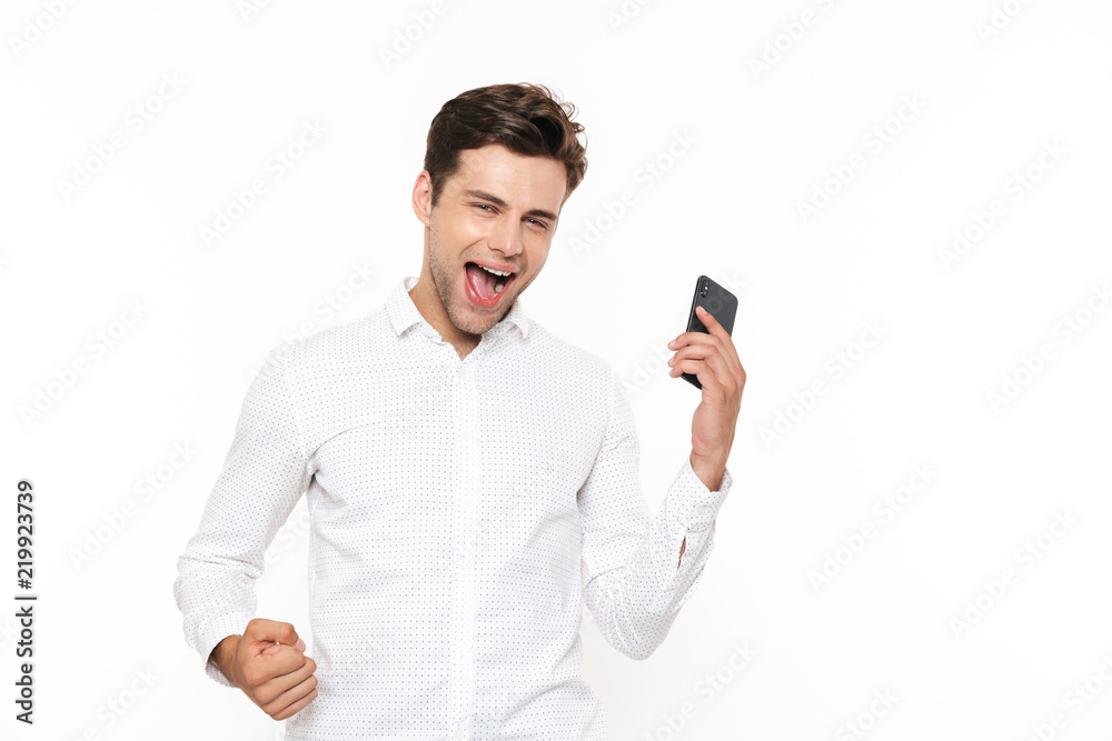 Poster Happy european man with short dark hair screaming while holding smartphone, isolated over white background