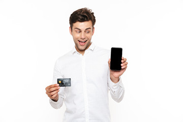 Handsome man with dark hair holding smartphone and credit card, isolated over white background