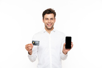 European guy with dark hair holding smartphone and credit card, isolated over white background