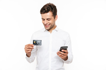 Brunette happy man with dark hair holding smartphone and credit card, isolated over white background