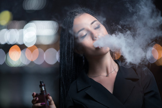 Woman smoking e-cigarette against night city lights background