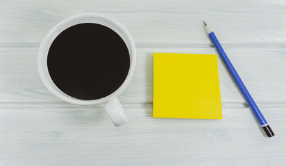Hot coffee in the morning write new ideas .Props decorations a blue pencil and yellow notebook on a white wooden floor background,.Top view Copy Space..