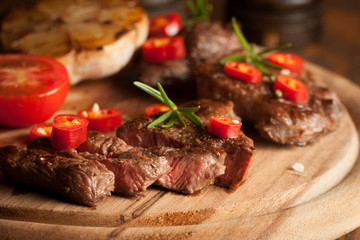 grilled fillet steak with tomatoes and roast vegetables on an old wooden board, background.