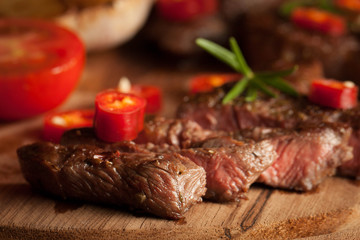 grilled fillet steak with tomatoes and roast vegetables on an old wooden board, background.