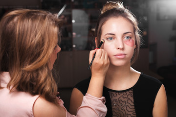 makeup woman applying a make up on a young model wearing hydrogel treating eye patches. concept of professional skin care