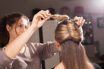 Fototapeta premium professional hairdresser making an unusual coiffure to a brown haired young model in a beauty salon