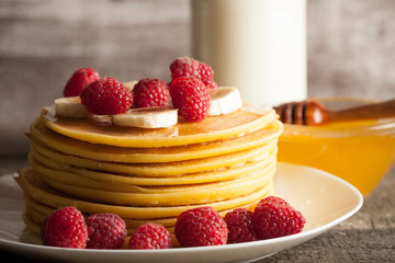 Tasty pancakes with blackberries, banana, raspberries, eggs, honey and maple syrup on wooden background. Morning breakfast concept.