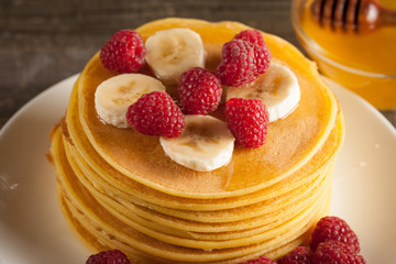 Tasty pancakes with blackberries, banana, raspberries, eggs, honey and maple syrup on wooden background. Morning breakfast concept.