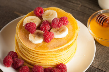 Tasty pancakes with blackberries, banana, raspberries, eggs, honey and maple syrup on wooden background. Morning breakfast concept.