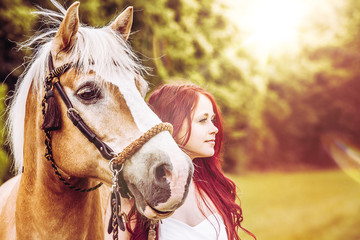 red-haired woman with brown horse in the sunset