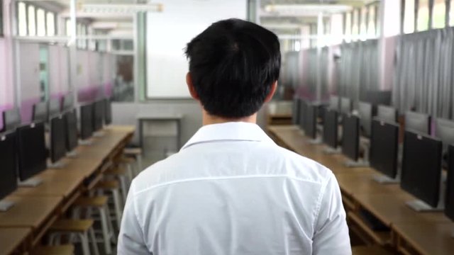Follow shot of back of young man in white shirt walking into computer laboratory room