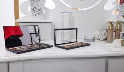 There are different powders and palettes with eye shadows on a table in a make up studio.