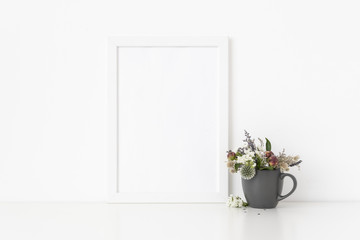 White a4 portrait frame mockup with dried field wild flowers in gray mug on white wall background. Empty frame, poster mock up for presentation design. Template frame for text, lettering, modern art.