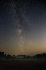 Starry night sky in the northern hemisphere. View of the Milky Way over a meadow with fog. Long...