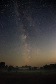 Starry night sky in the northern hemisphere. View of the Milky Way over a meadow with fog. Long exposure.