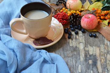 Flat lay of composed cup with black coffee on wood table with ripe berries of rowan and dark foliage. Cappuccino or latte or tea on a vintage table. fallen leaves, ripe apples, berries. Copy space
