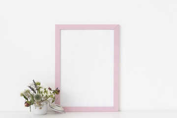 Minimal pink portrait frame mockup with dried field wild flowers in pot on white wall background. Empty frame, poster mock up for presentation design. Template frame for text, lettering, modern art.