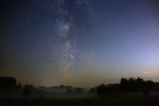 Starry night sky in the northern hemisphere. View of the Milky Way over a meadow with fog. Long exposure.
