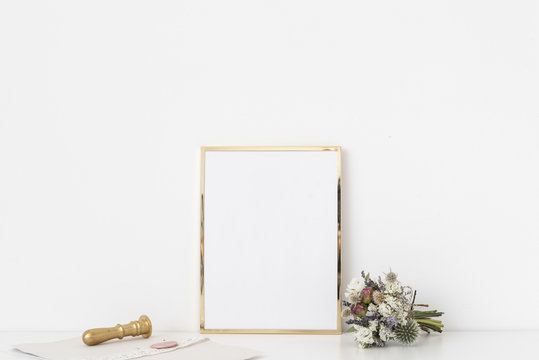 Gold a4 portrait frame mockup with small bouquet of dried flowers and gold stamp on white wall background. Empty frame, poster mock up for presentation design.
