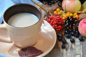 Flat lay of composed cup with black coffee on wood table with ripe berries of rowan and dark foliage. Cappuccino or latte or tea on a vintage table. fallen leaves, ripe apples, berries. Copy space
