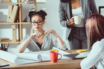 Serious asian businesswoman in eyeglasses sitting at table with colleagues and working in office