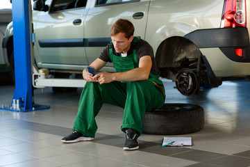 A young mechanic in a green overalls sits on a wheel in service