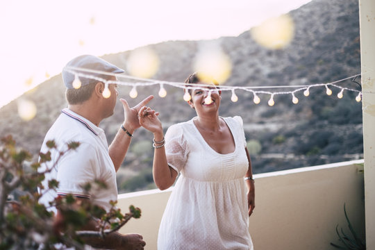happy caucasian people dancing together at home in terrace with lights during the sunset. romantic and relationship concept image for happy people in outdoor leisure activity about love