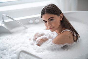 Portrait of serene girl looking at camera while having leisure in cozy bath. Orderly female during relaxing procedure concept