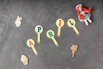 The inscription "April" from children's educational plastic cards with letters, alphabet, abc. A funny knitted doll with red hair is a gift for the fools' day on the 1st of April.