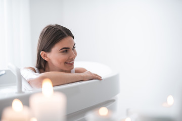 Obraz na płótnie Canvas Portrait of happy pretty woman with attractive smile relaxing while taking bath in bright apartment during romantic atmosphere. Copy space