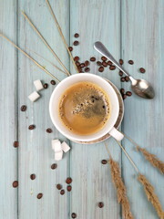 A cup of coffee with sugar, coffee spoon and spikelets on a soft blue painted wooden background. Flat lay photo of morning coffee in the village