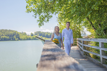 Lovely couple in love walking over the bridge. Sexy blonde in attractive dress with deep cleavage has a nice bouquet of yellow flowers.