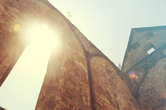 The sun is shining through one of the windows in a church. There is no more ceiling and roof in there.