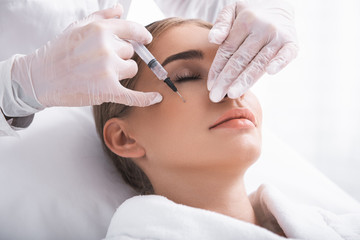 Obraz na płótnie Canvas Staying calm. Attractive girl with closed eyes having skincare procedure at beauty salon. Cosmetologist hands in sterile gloves with syringe doing mesotherapy
