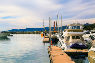 Fototapeta na wymiar Luxury yachts moored at pier in sea port at sunset, back view. Marine dock of modern motor and sailing boats, blue water sea. Travel and fashionable vacation.