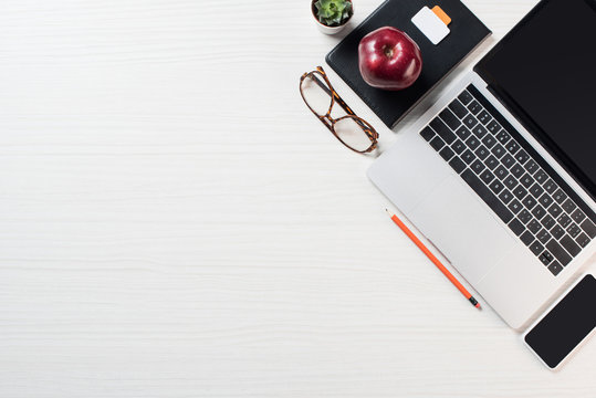 elevated view of eyeglasses, apple, smartphone and laptop on table