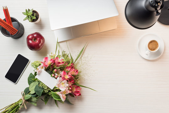top view of workplace with greeting card with flowers, laptop, coffee and smartphone on table - Powered by Adobe
