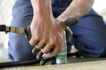 Worker's hands holding a drill making holes on a body plane for further riveting